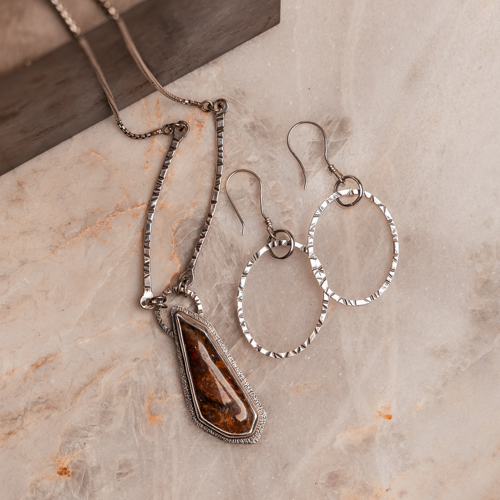 Bohemian-style silver earrings and gemstone necklace with textured ovals and artisanal craftsmanship